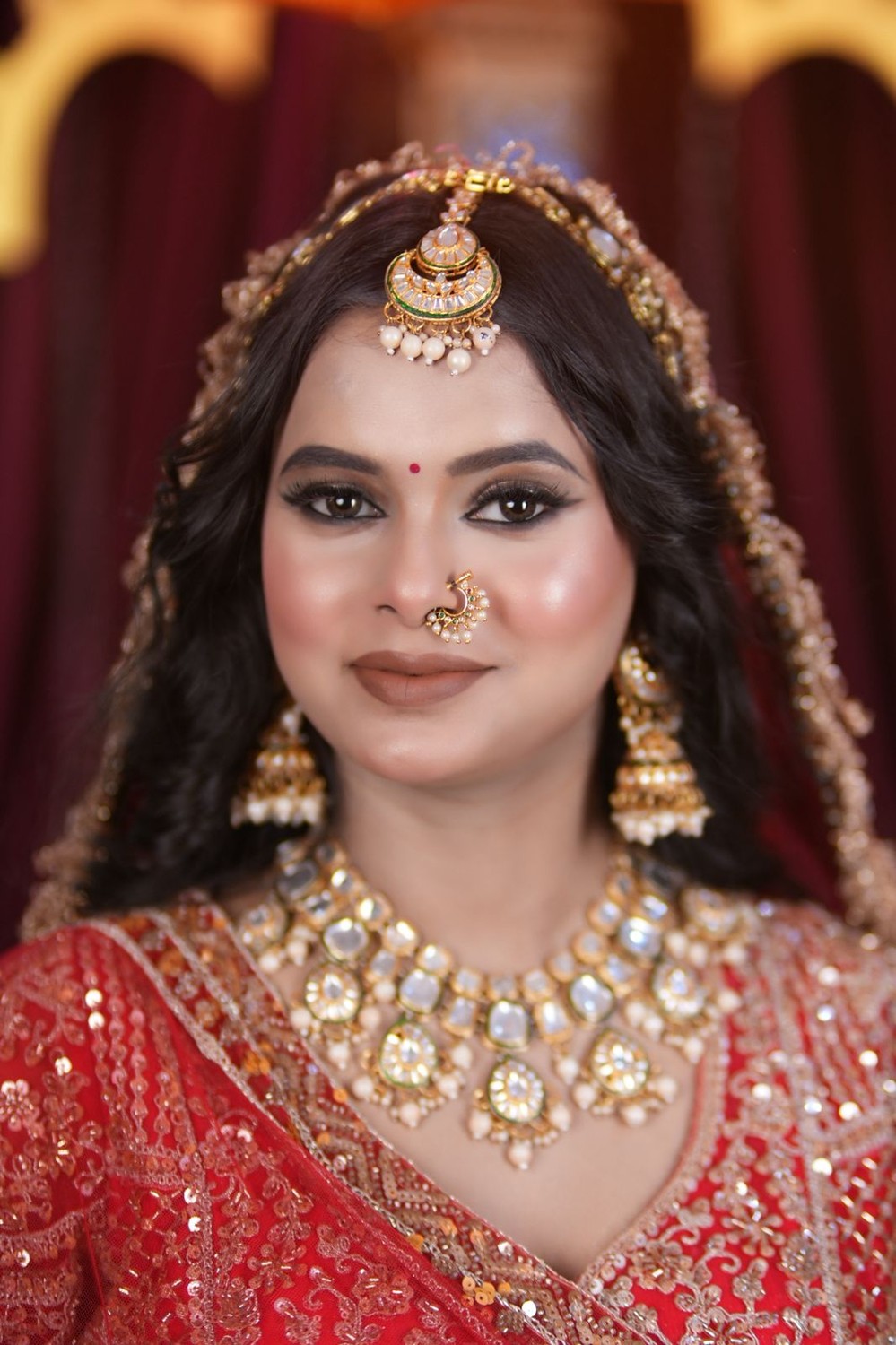 Bride in a rich red bridal lehenga with statement gold jewellery, dramatic HD bridal makeup by Neha Verma Artist