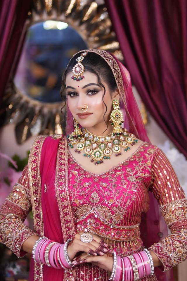 Bride in a magenta bridal lehenga with kundan jewellery and mathapatti, posed before a round mirror backdrop