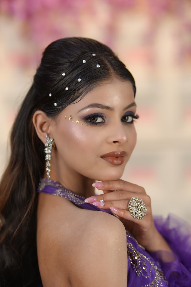 Model in a purple gown with delicate face gems and a statement ring, soft glam makeup